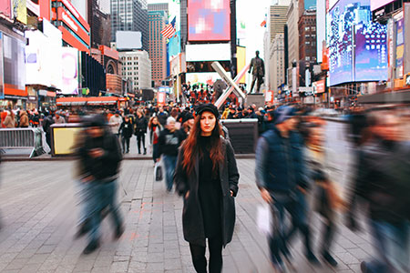 A female stands still in Times Square, with people and traffic all around her