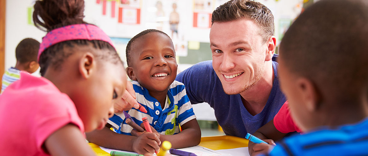 A male teacher smiles with his students during art time