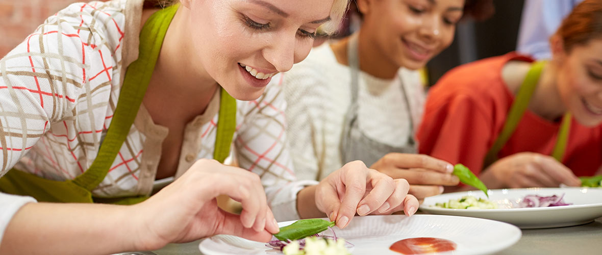 A female teacher demonstrates for her FCS students how to properly prepare an attractive dish in a culinary class.