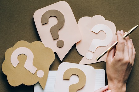 On top of a notebook, there are 4 paper question marks. 